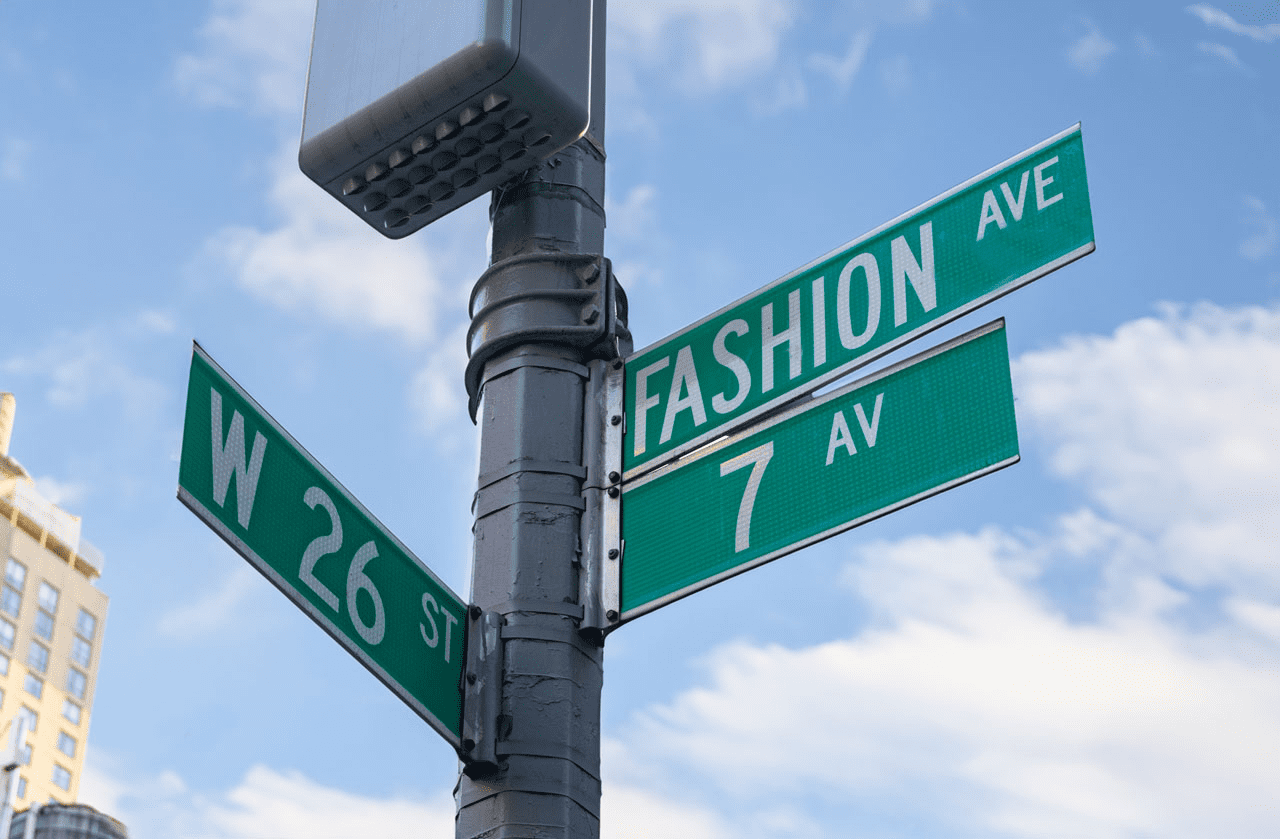 Street signs marking the intersection of Fashion Avenue and West 26th Street against a blue sky.