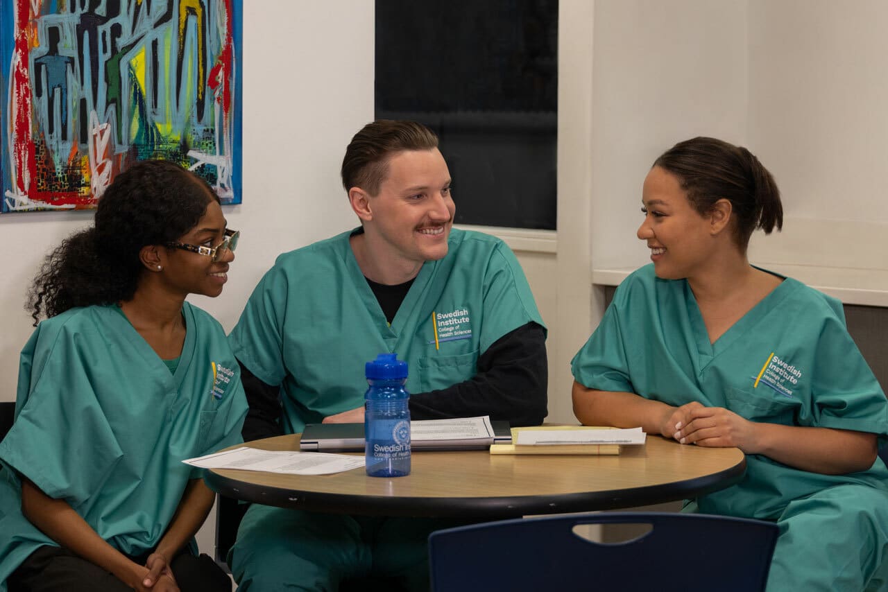 three Swedish institute students in their uniforms sitting at a table