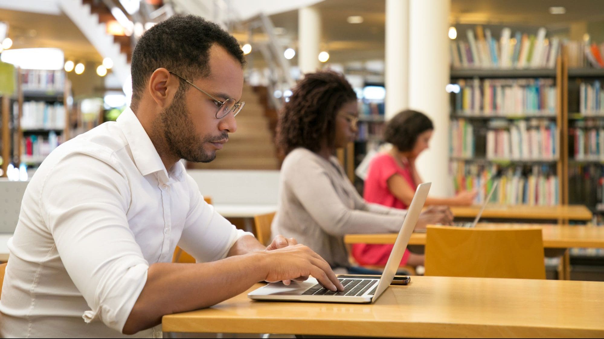 a man and two women in the library working on laptops. accreditation approvals