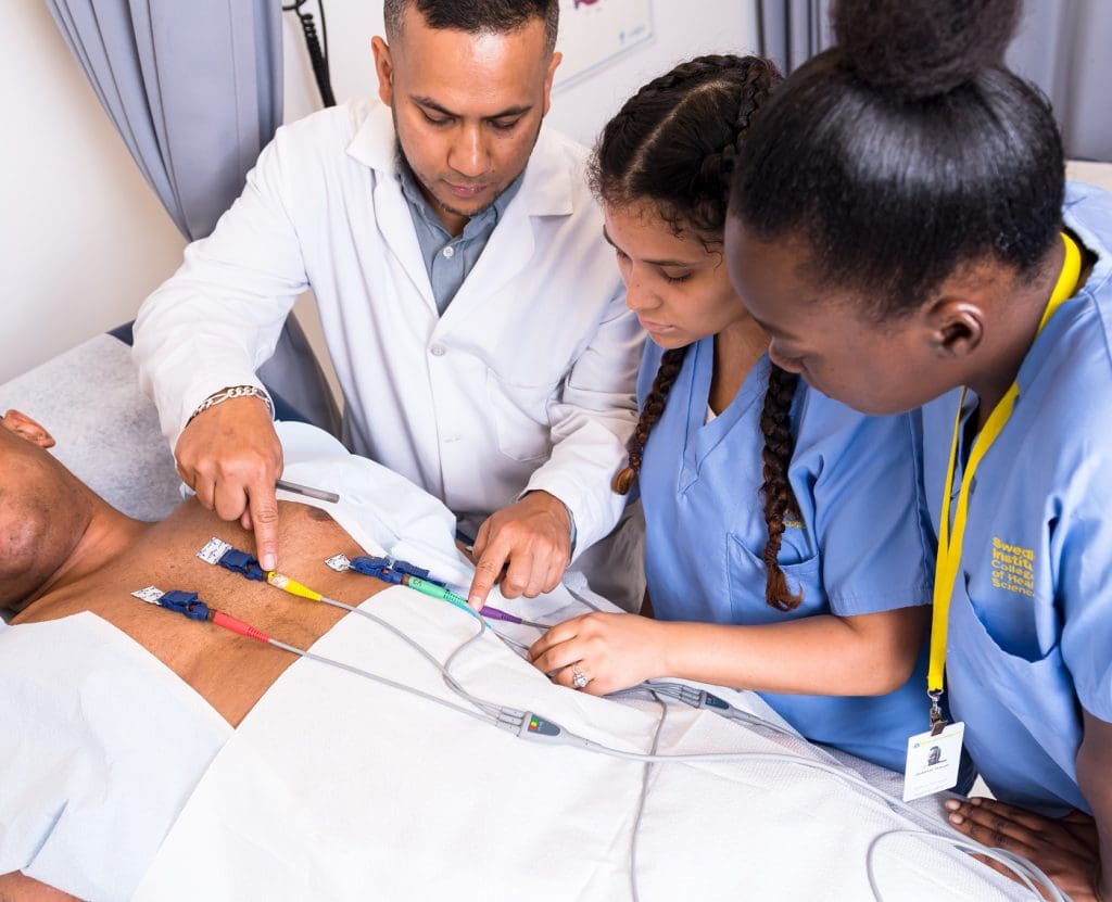 A Swedish Institute instructor explaining how to find success with an EKG machine to two medical assistant students